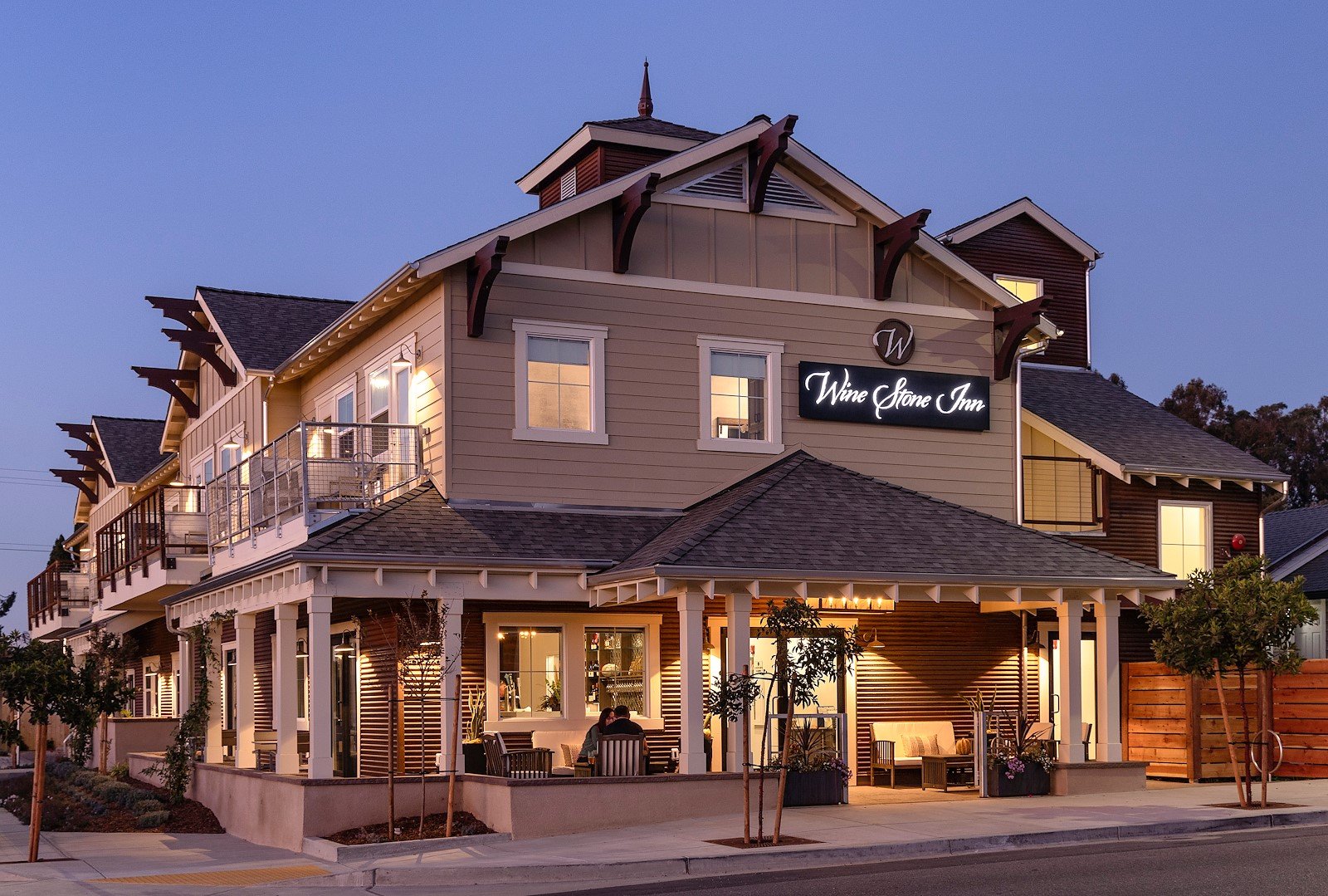 The Wine Stone Inn at dusk: a two-storey craftsman building with a wraparound porch, lit from inside