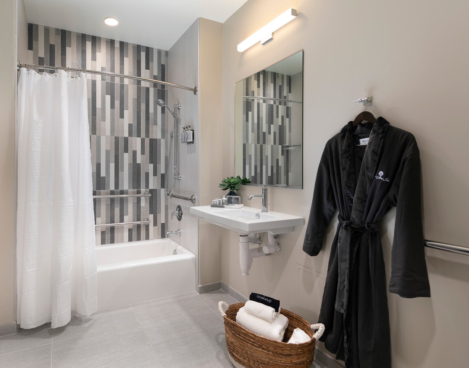 ADA bathroom with a bathtub, bench and grab bars, and a robe hanging